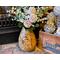 A handmade sunflower vase,  filled with faux daisies and zinnias, decorates a fireplace hearth. The vase is made from a dried gourd. 